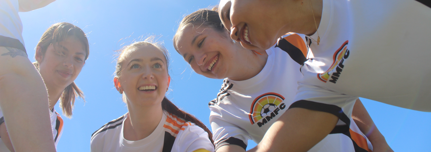 a group of young women are huddled together, wearing white soccer shirts, smiling
